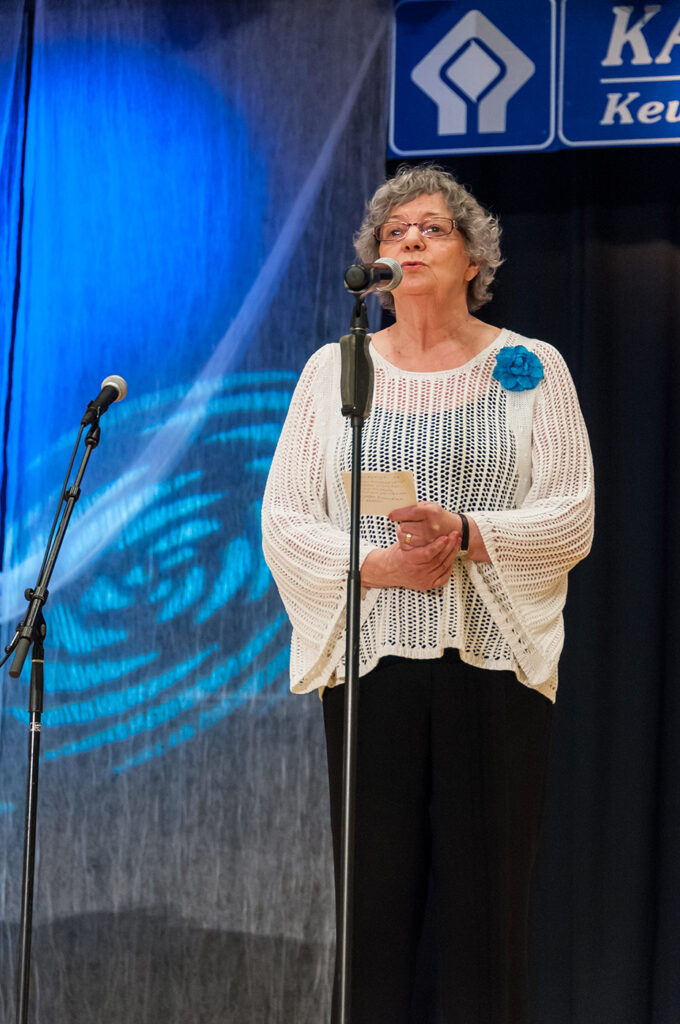 Valkopuseroinen nainen seisoo esiintymislavalla ja lausuu runoa mikrofoniin.