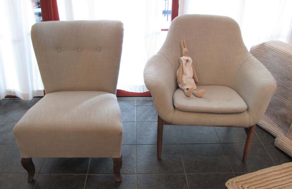 Kuvassa kaksi vaalealla kankaalla verhoiltua nojatuolia. Toiselle tuolille on aseteltu kankaasta ommeltu pupuhahmo.