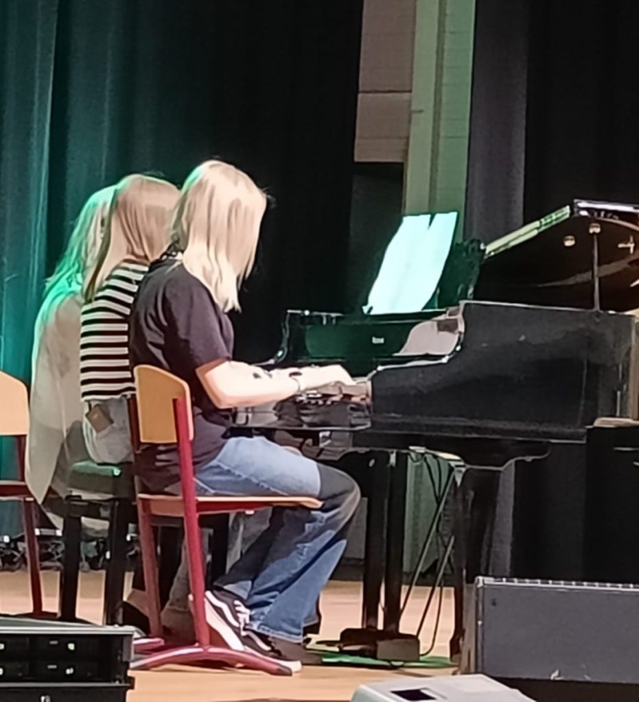 Kaksi nuorta ja aikuinen soittavat samaa pianoa.