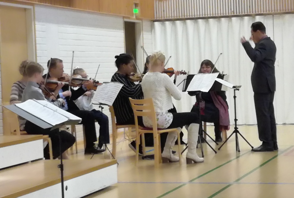 Kahdeksan viulunsoittajaa esiintyy istualtaan, mies johtaa orkesteria.