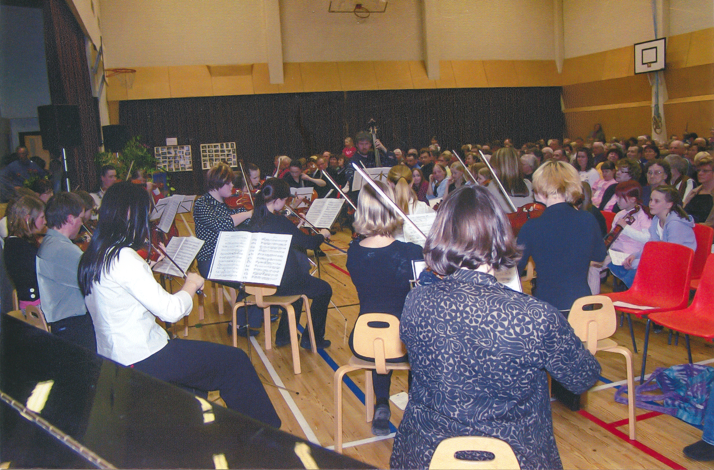 Orkesteri esiintyy koulun juhlasalissa, kuva on otettu orkesterin takaa yleisöön päin.