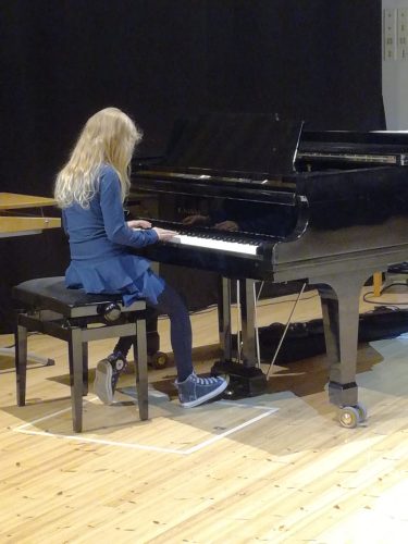Tyttö istuu selin kameraan soittamassa pianoa.