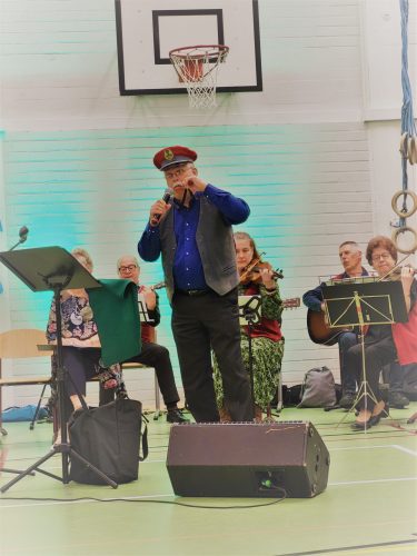 Mies konduktöörin lakki päässä laulaa pelimannien säestyksellä