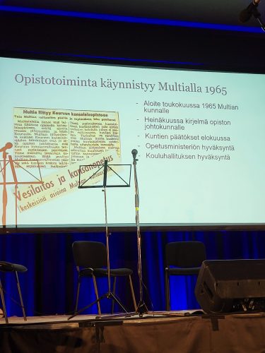 Lehtiartikkeli ja selostus Multian osaston aloitusvaiheesta heijastettuna valkokankaalle.