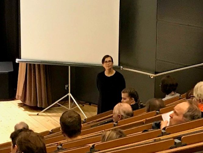 Nainen seisoo auditorion alaosassa katsoen yleisöön päin.
