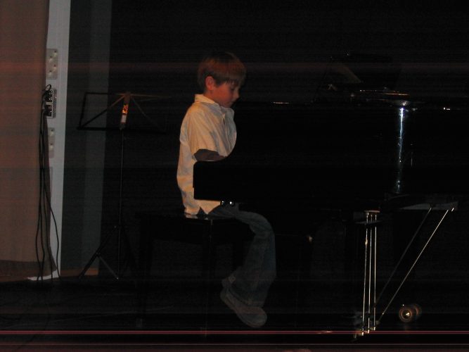 Poika valkoisessa paidassa soittaa pianoa.