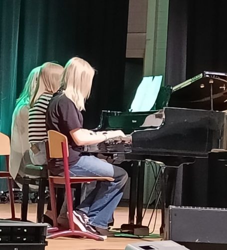 Kaksi nuorta ja aikuinen soittavat samaa pianoa.