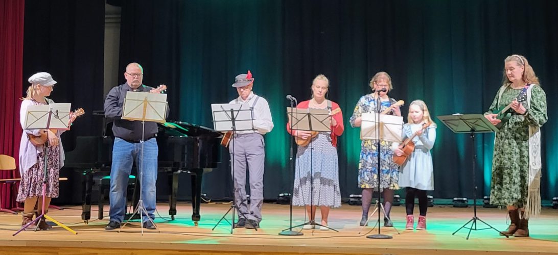 Seitsemän hengen ryhmä soittaa ukulelea esiintymislavalla.