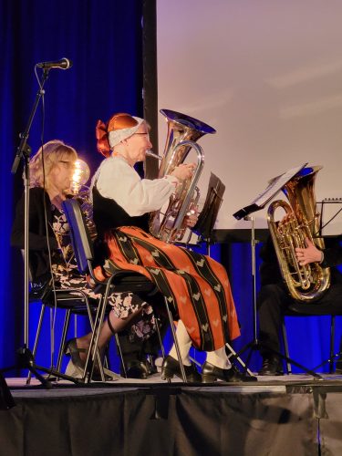 Kansallispukuinen nainen istuu ja soittaa baritonitorvea.