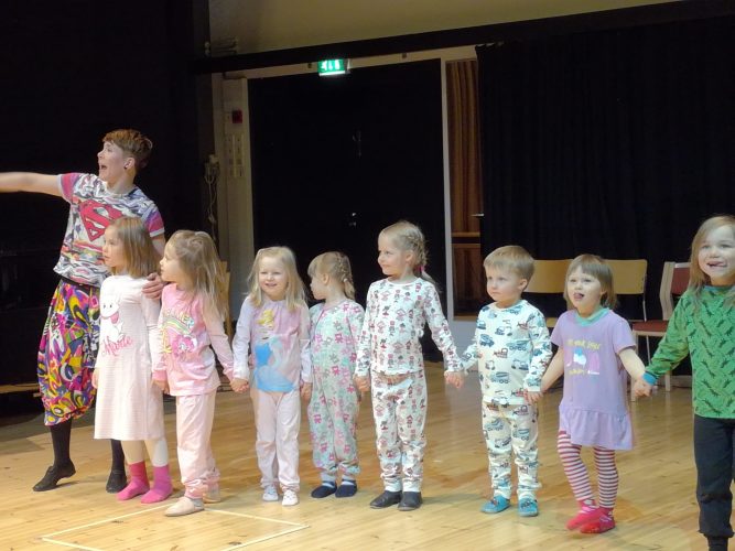 Kahdeksan pikkulasta pyjamissa esityksen loppukumarruksessa ohjaajansa kanssa.