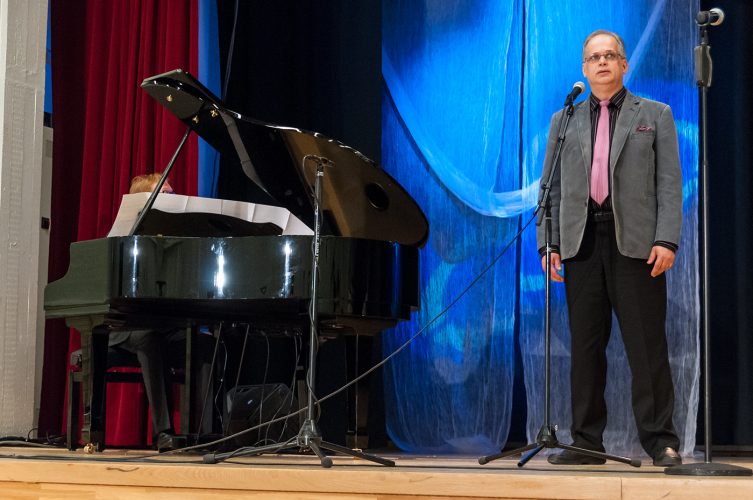 Mies harmaassa puvuntakissa laulaa mikrofoniin ja toinen mies soittaa vieressä pianoa.