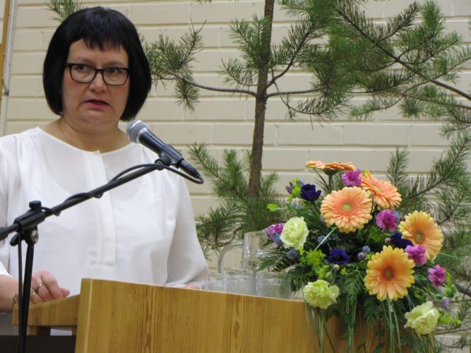 Tummahiuksinen nainen juontaa ohjelmaa puhujapöntössä.